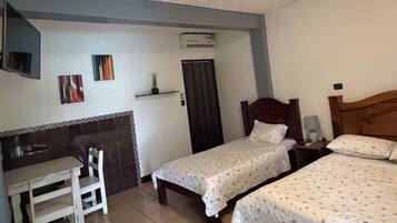A room with two beds, a desk, a chair, and a small table with a potted plant.