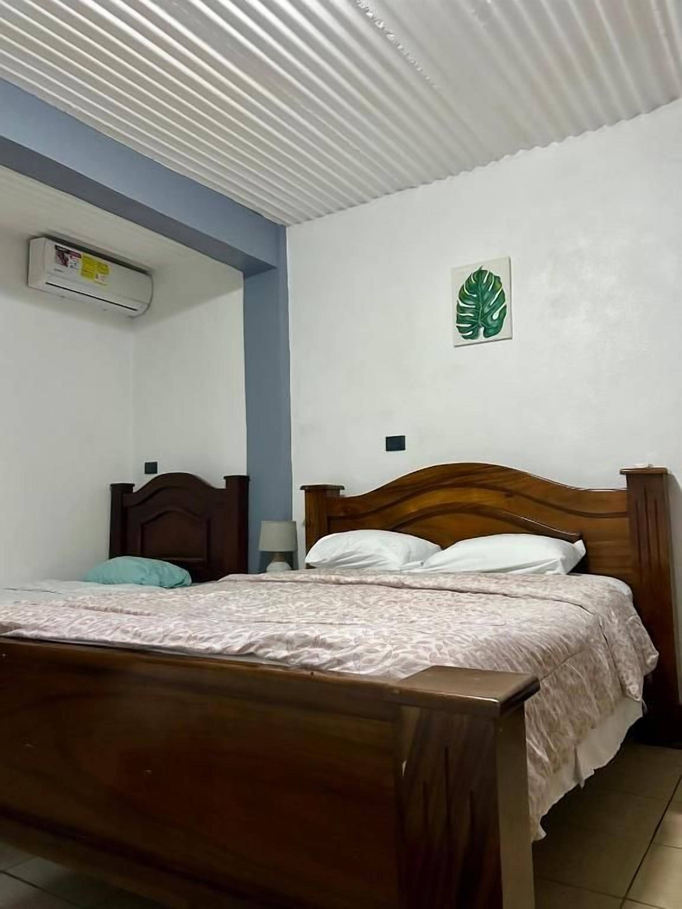 Un dormitorio con una cama de madera, aire acondicionado instalado en la pared y un adorno con una hoja verde.