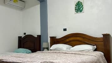 Un dormitorio con una cama de madera, aire acondicionado instalado en la pared y un adorno con una hoja verde.