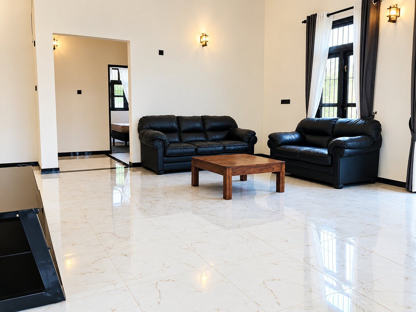 A spacious living room with two black leather sofas, a wooden coffee table, and a tiled floor.