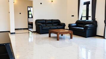 A spacious living room with two black leather sofas, a wooden coffee table, and a tiled floor.