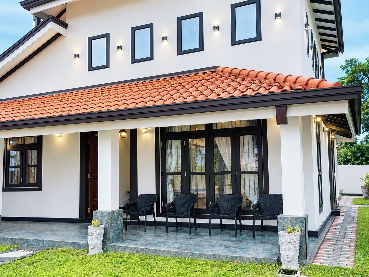 Una casa moderna con techo de tejas, ventanas amplias y mobiliario exterior.