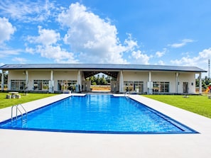 A swimming pool with a covered pavilion, a clear sky, and a grassy area.