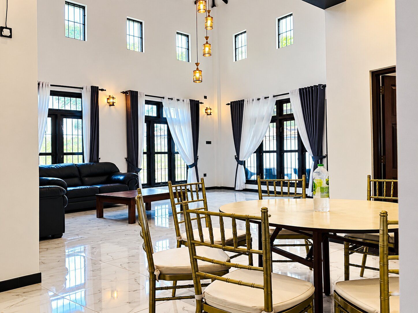A spacious room with a dining table, chairs, a sofa, and a large window with curtains.