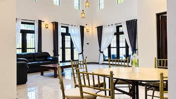 A spacious room with a dining table, chairs, a sofa, and a large window with curtains.