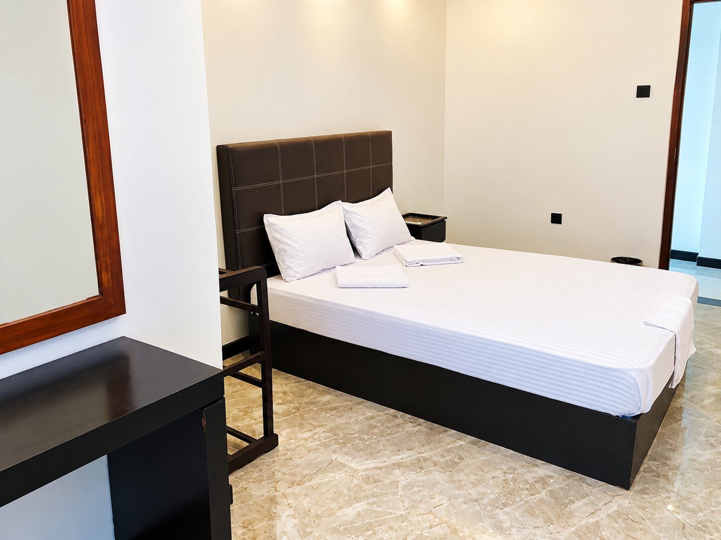 Una habitación de hotel con cama, mesita de noche, espejo y puerta.