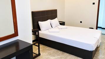 Una habitación de hotel con cama, mesita de noche, espejo y puerta.