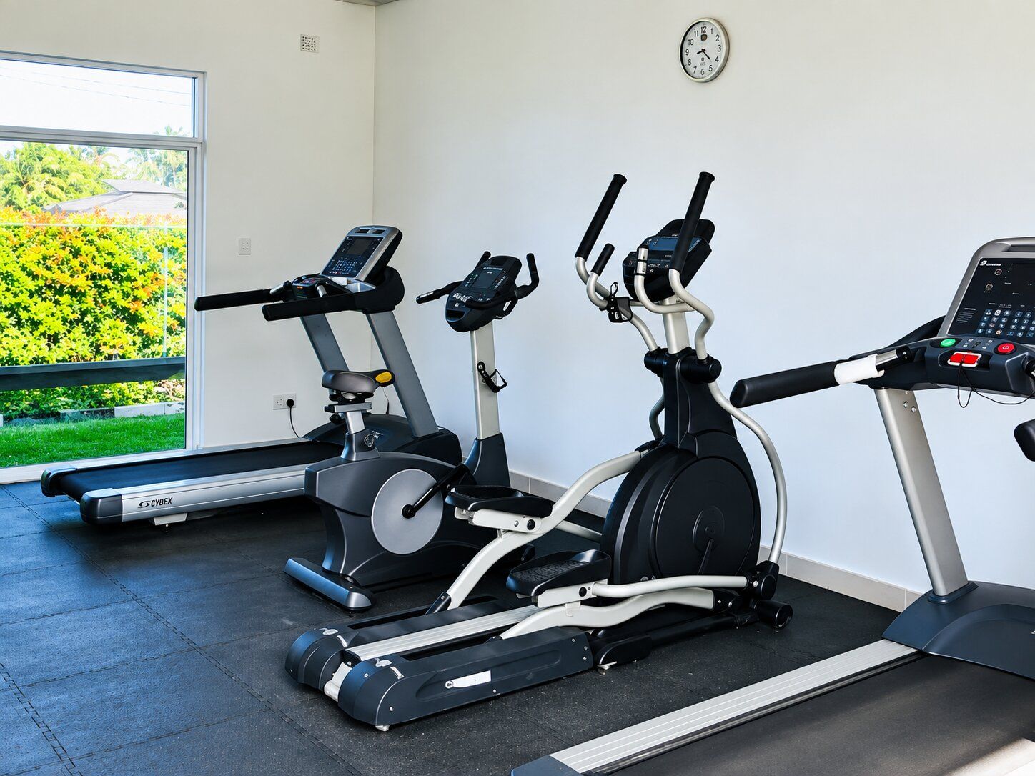 Un gimnasio con tres bicicletas estáticas, una cinta de correr y un reloj de pared.
