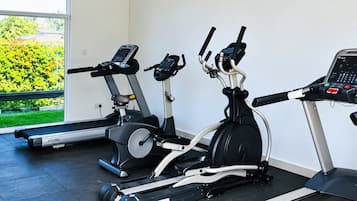 Un gimnasio con tres bicicletas estáticas, una cinta de correr y un reloj de pared.