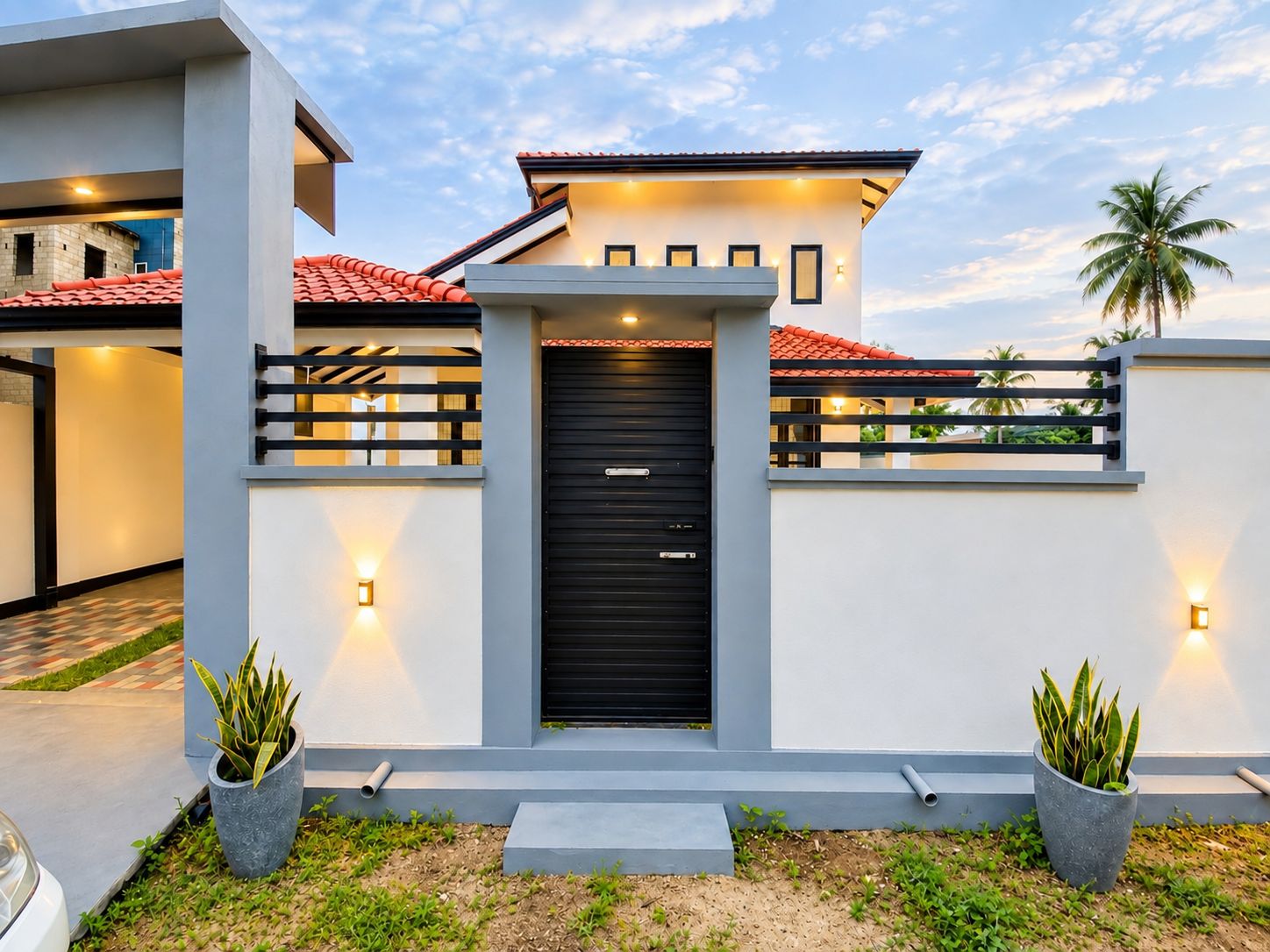 A modern two-story house with a black front door, a balcony, and two potted plants.