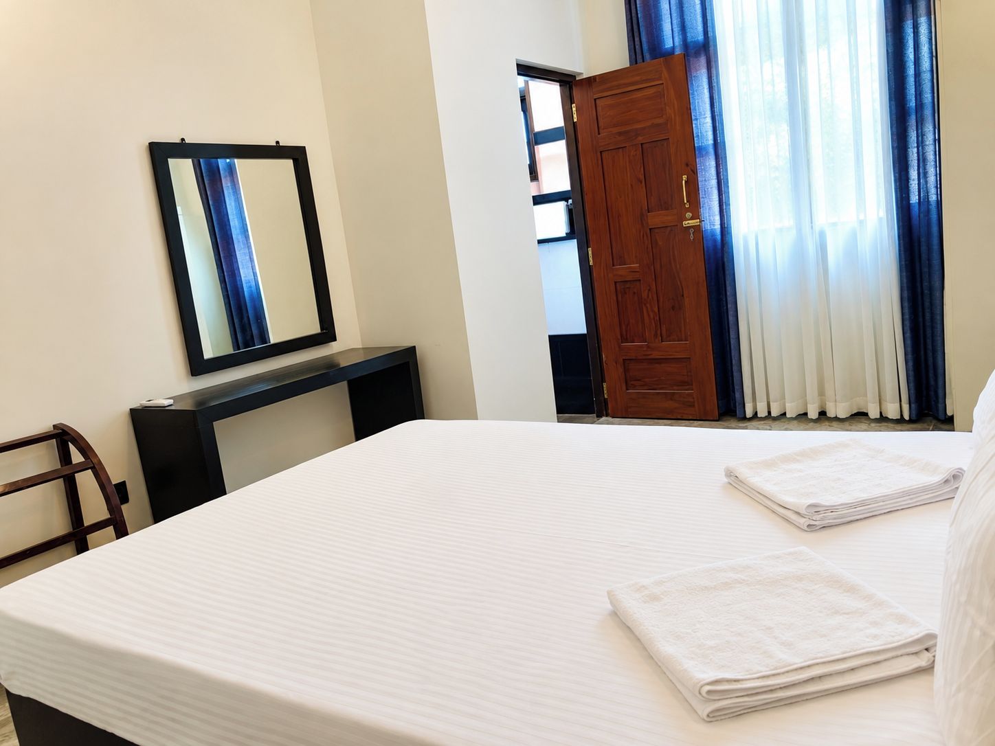 Habitación de hotel con cama, escritorio, espejo, puerta y ventana con cortinas.