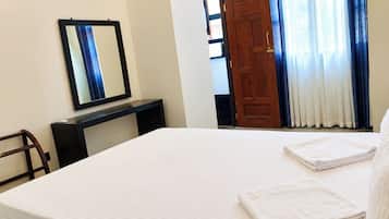 Habitación de hotel con cama, escritorio, espejo, puerta y ventana con cortinas.