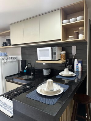 Una cocina moderna con encimera negra, electrodomésticos blancos y estante de madera arriba.