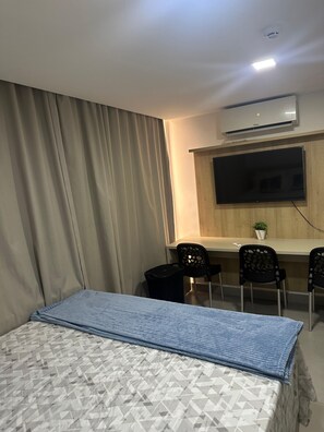 Ein Hotelzimmer mit einem Bett, einem Schreibtisch mit Stühlen, einem Flachbildfernseher und einer Klimaanlage.