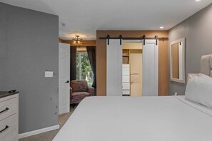 A bedroom with a bed, a chair, a wardrobe, and a door leading to another room.