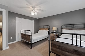 Ein Schlafzimmer mit zwei Betten, deren Rahmen aus Metall gefertigt sind, einem Deckenventilator und einer Tür zu einem weiteren Raum.
