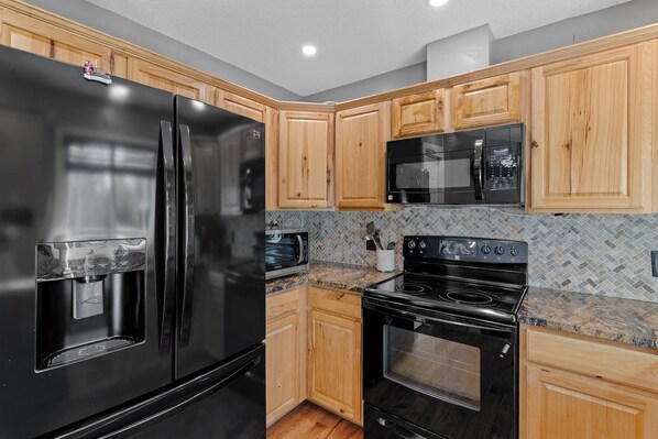 A kitchen with a black refrigerator, a microwave, and an oven.