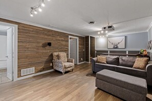 A modern living room with a wooden accent wall, a grey sofa, a patterned armchair, and a ceiling projector.
