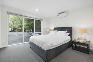 Ein modernes Hotelzimmer mit einem großen Bett, einem Nachttisch, einer Lampe und Blick durch eine Glastür.