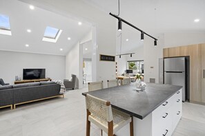Ett modernt kök med en central köksö, en matplats med stolar, en soffa och en tv i vardagsrummet.
