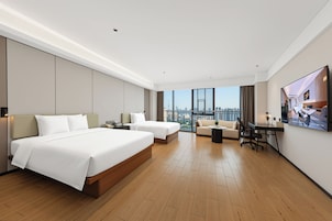 Ein modernes Hotelzimmer mit einem großen Bett, einem Einzelbett, einer Couch, einem Schreibtisch und Blick auf die Stadt.