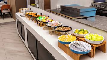 Buffet com diversos alimentos e cozinha moderna ao fundo.