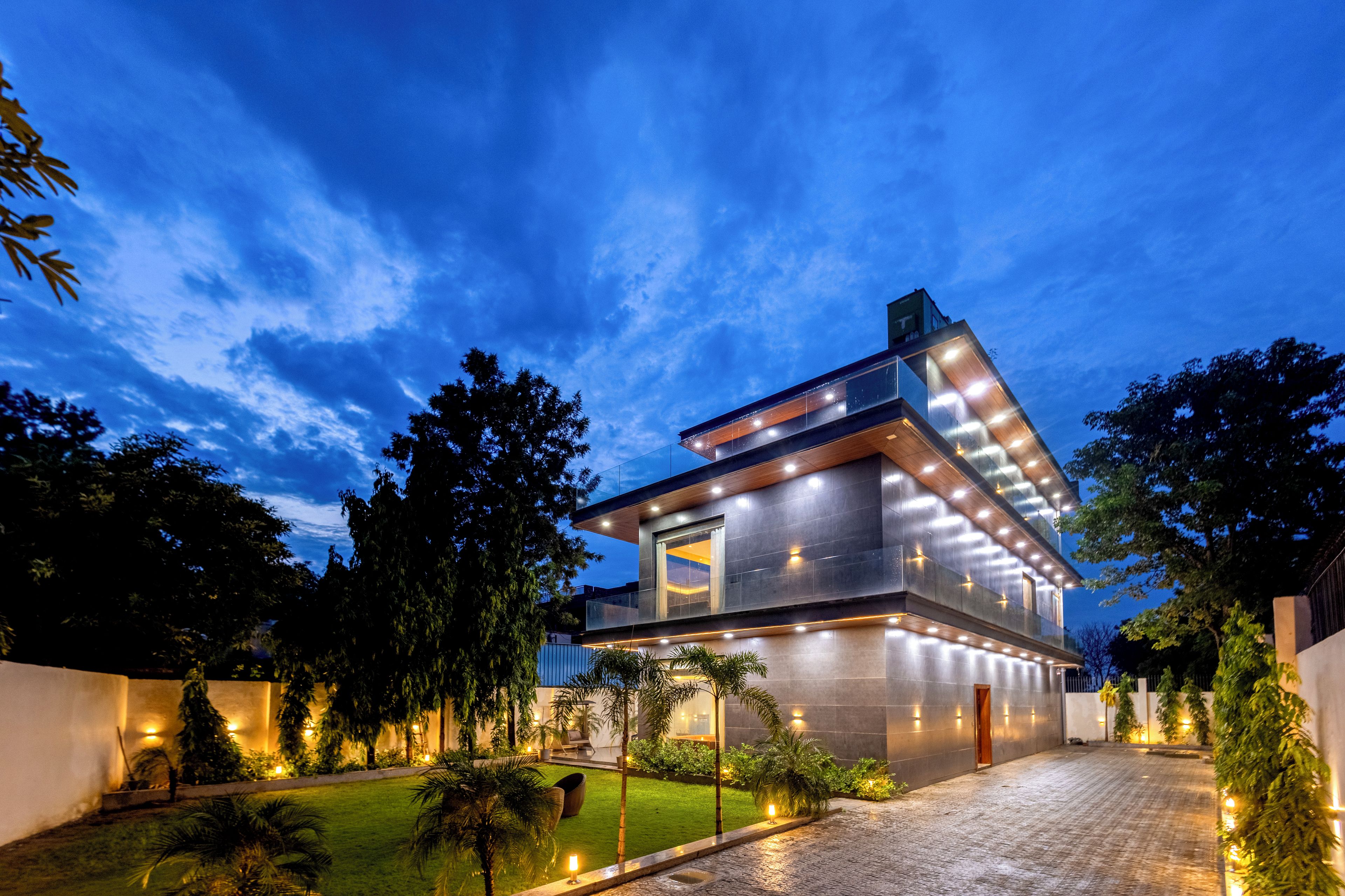 A modern two-story house with a flat roof, large windows, and a well-lit exterior.