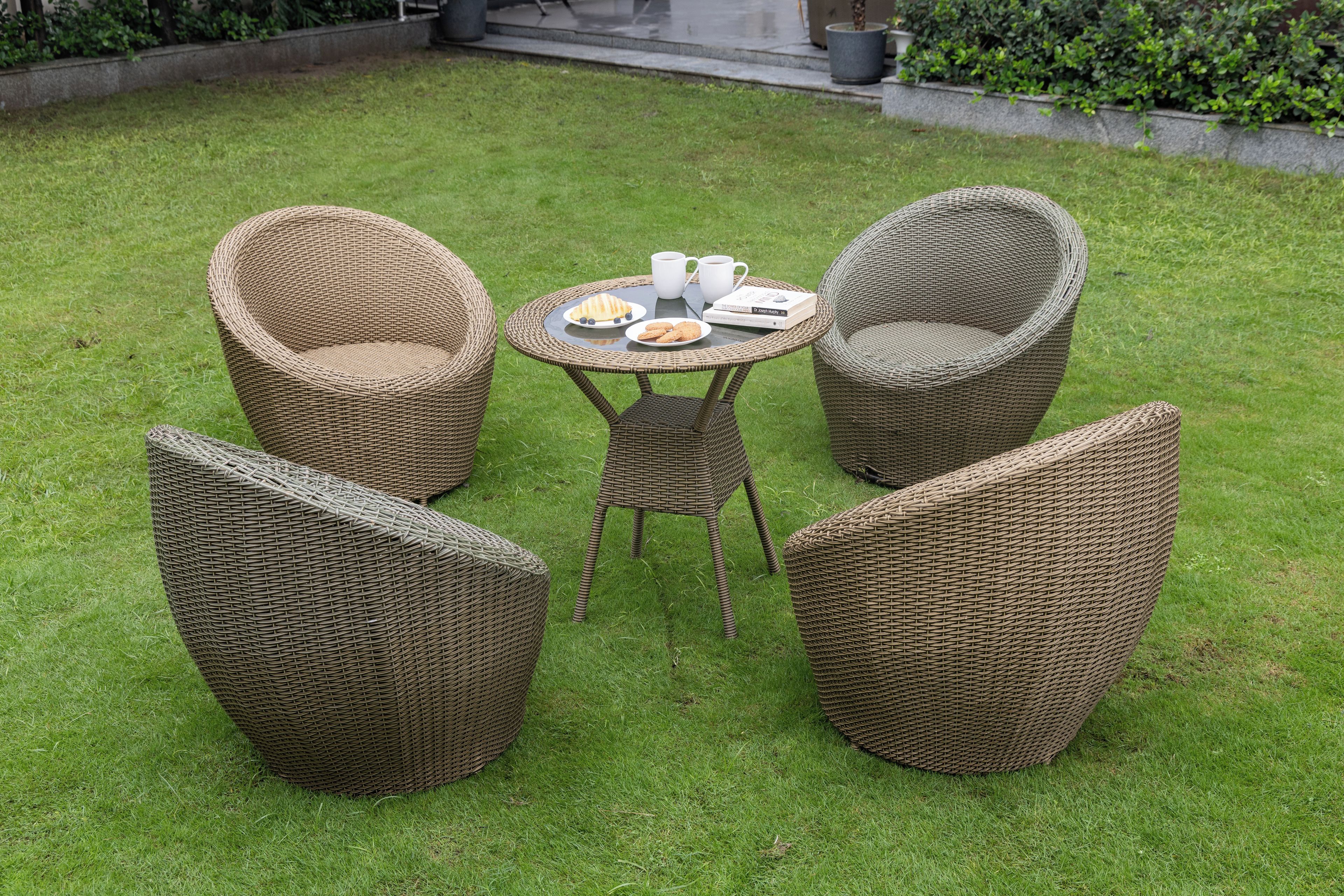 A garden with wicker furniture, including two chairs and a table with a book and a plate of food.