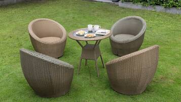 A garden with wicker furniture, including two chairs and a table with a book and a plate of food.