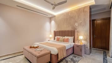 Un dormitorio con cama, mesitas de noche, ventilador de techo, puerta de madera y suelo de mármol.