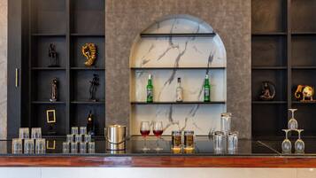 A bar area with shelves containing bottles and glasses, a marble wall with a curved arch, and a wooden counter.