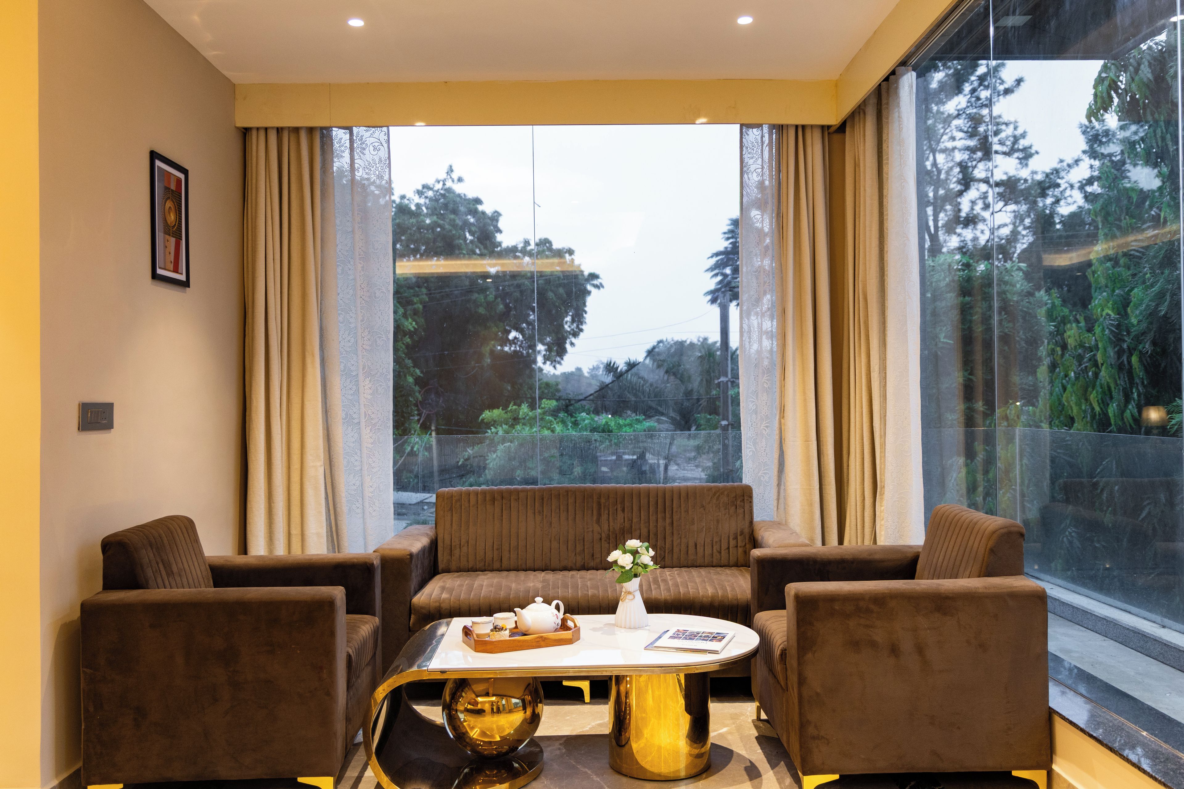 A modern living room with a sofa, two armchairs, a coffee table, and a view of trees through large windows.