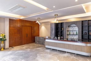 A reception area with a marble counter, wooden cabinets, and a modern light fixture. - ELIVAAS Signature DSG Farm 3BHK with Bar (New Delhi)