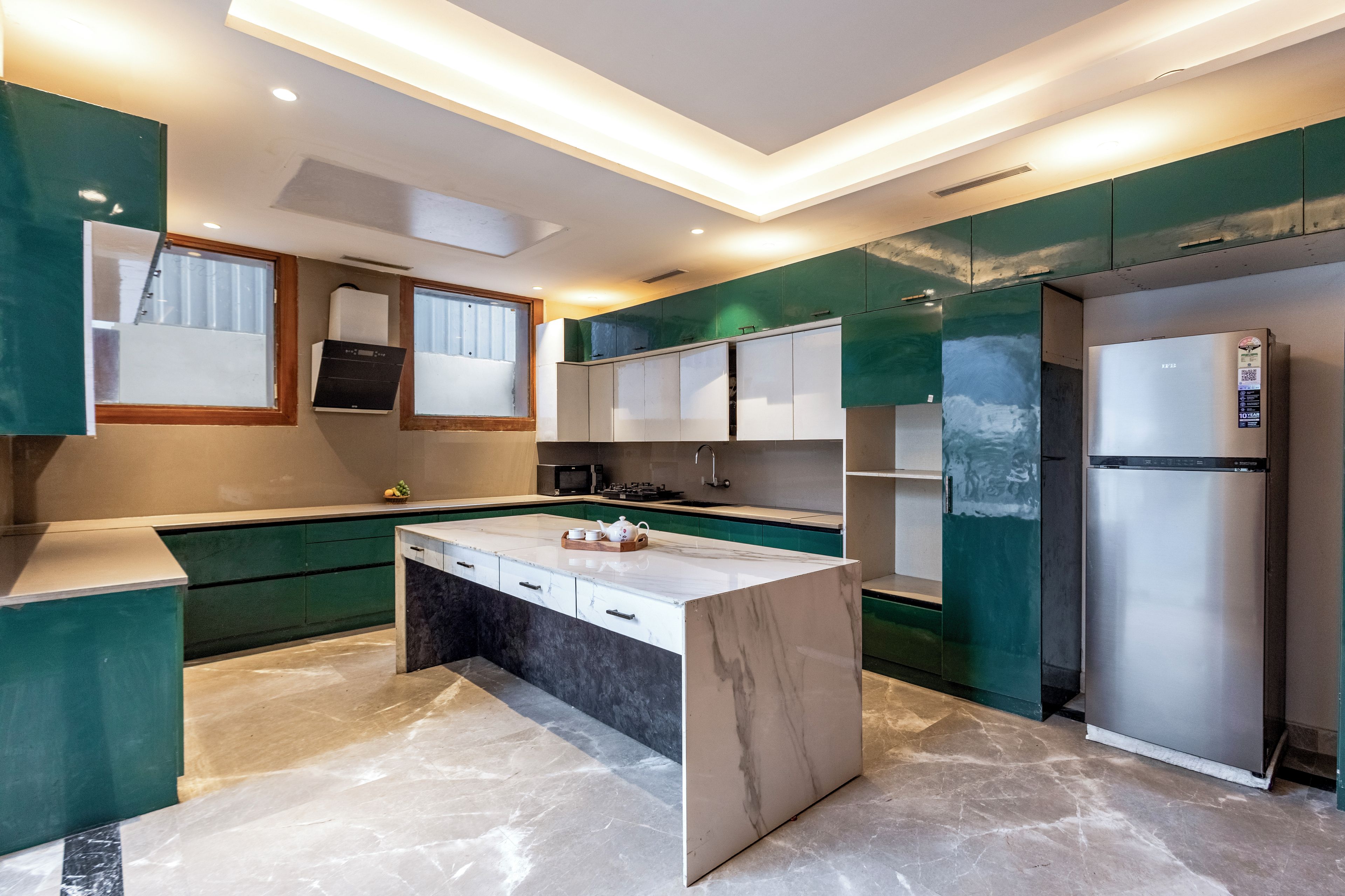 A modern kitchen with a central island, built-in appliances, and green cabinetry.