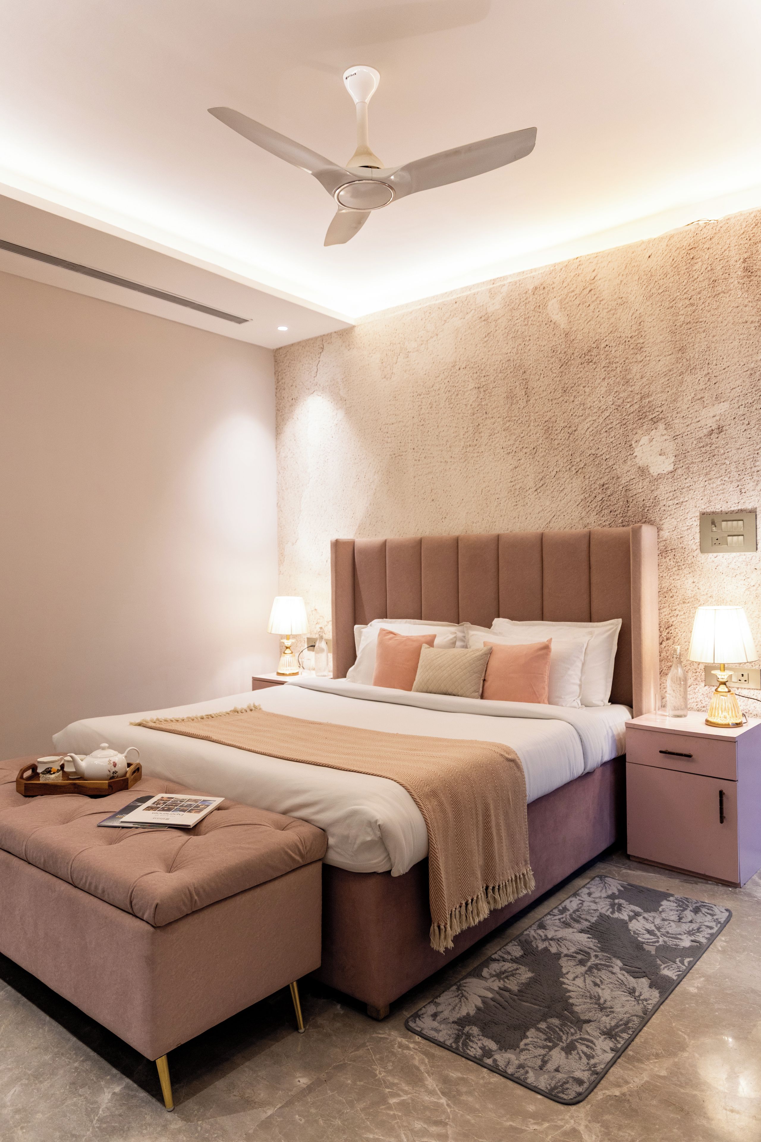 A modern bedroom with a large bed, bedside tables, a ceiling fan, and a decorative rug.