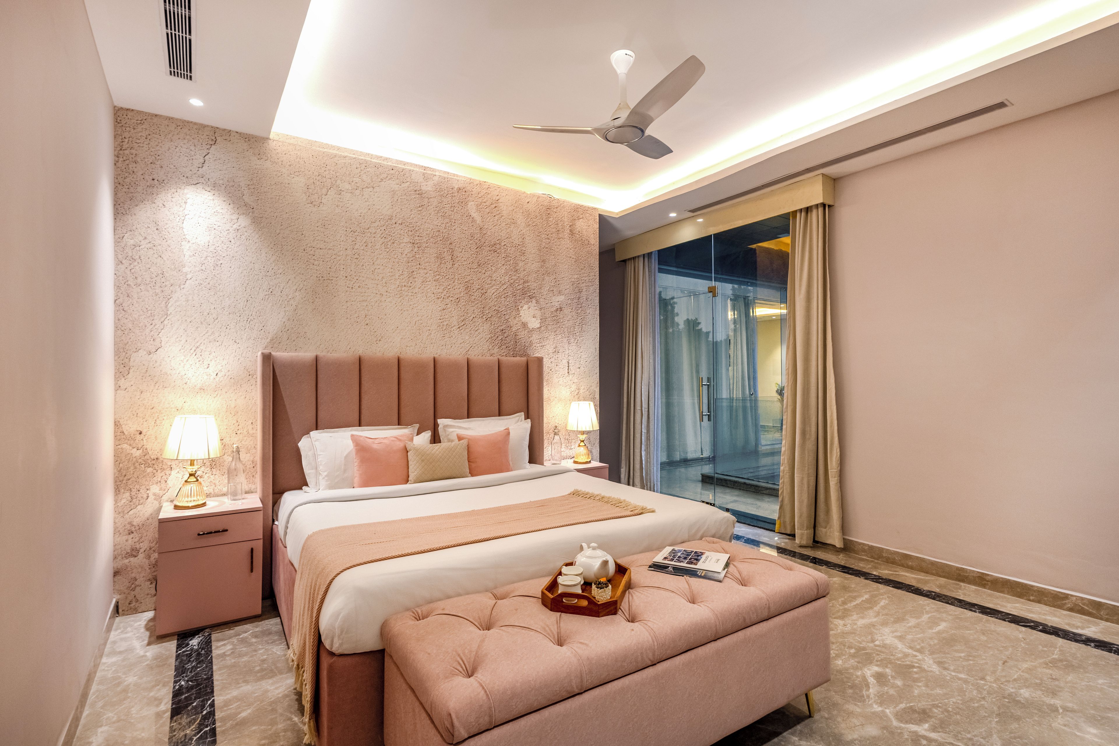 A modern bedroom with a large bed, a ceiling fan, a glass shower, and a marble floor.