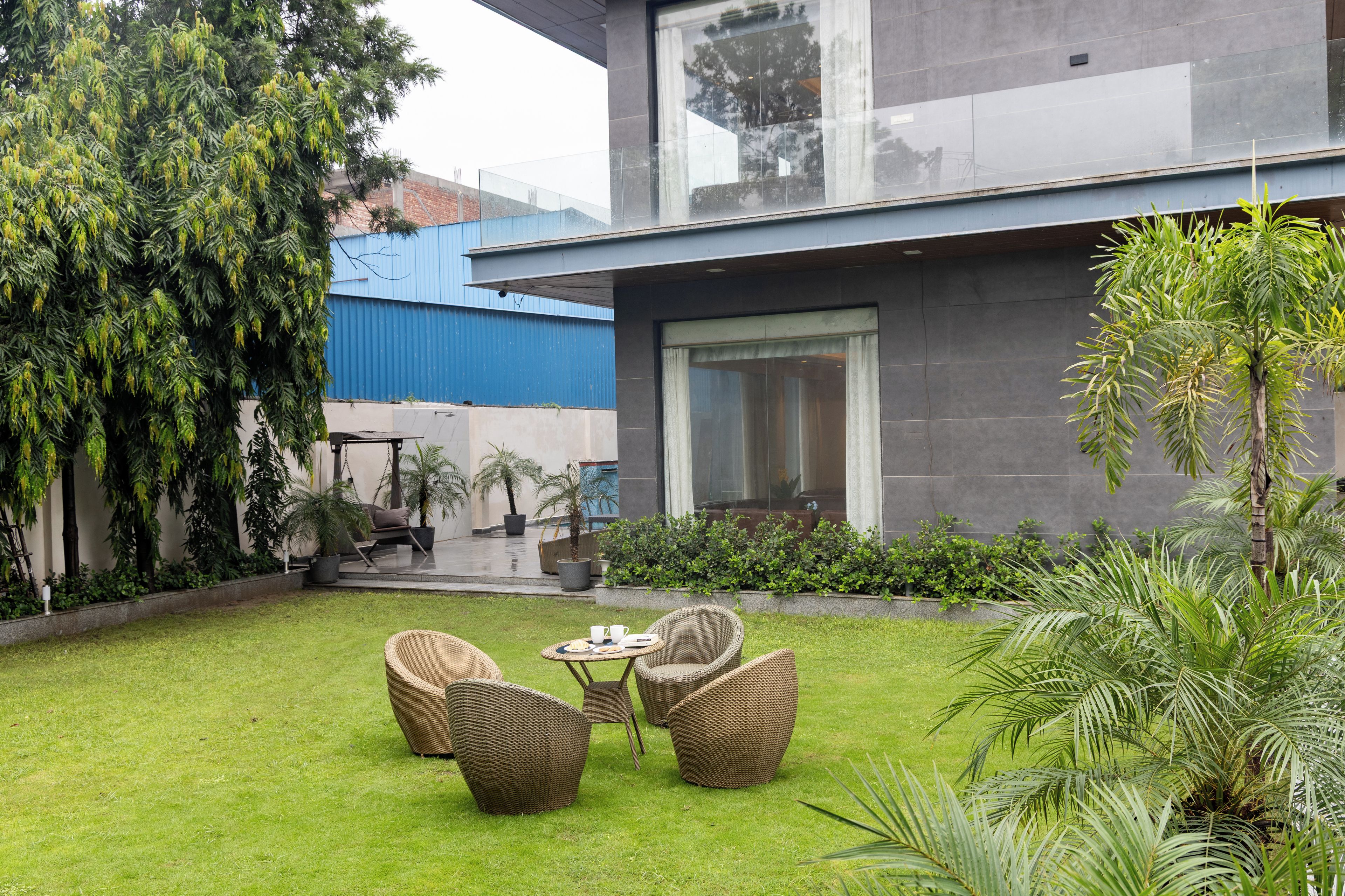 Une maison moderne dotée d’un patio aménagé avec des meubles en osier, une petite table et des plantes en pot.