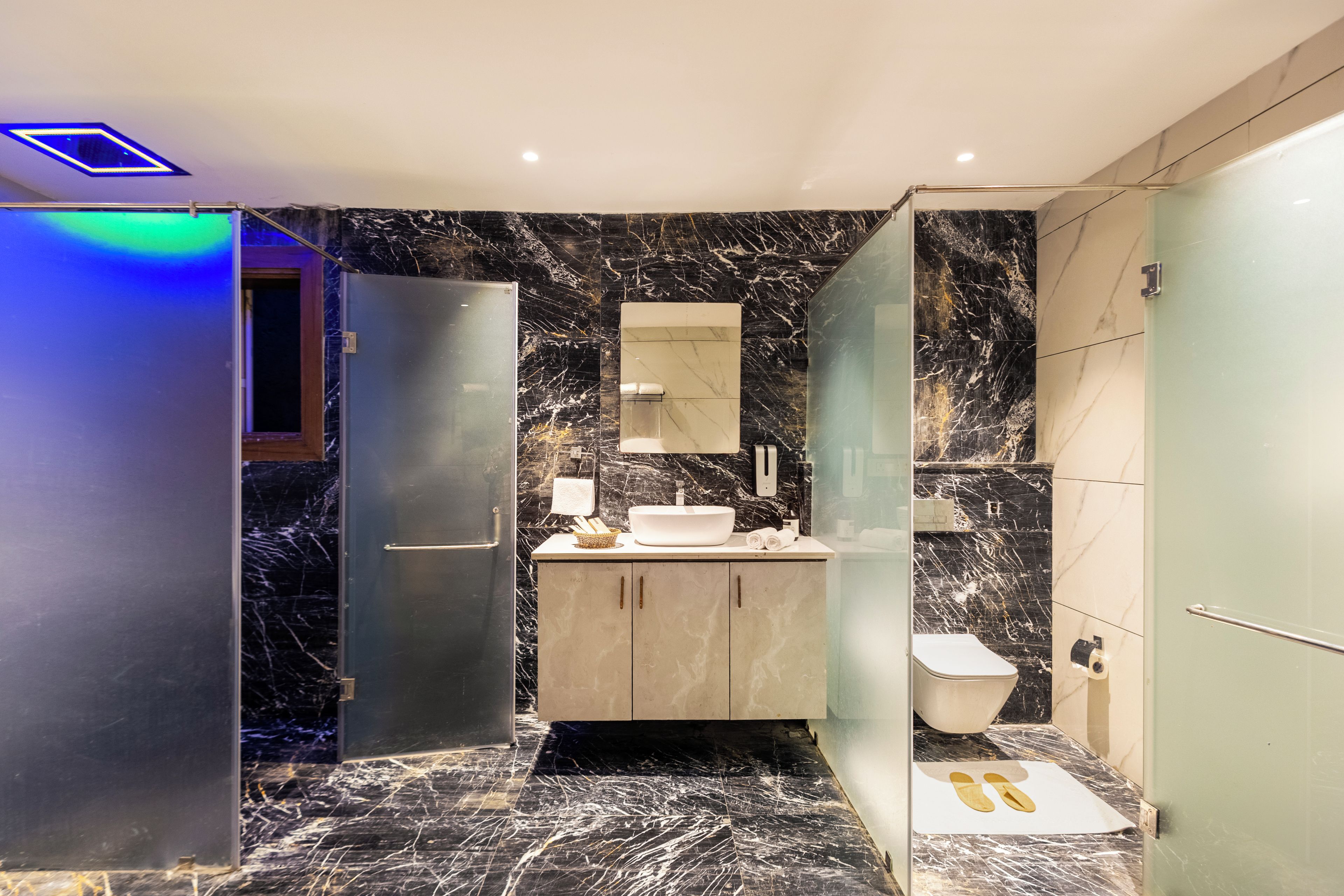 Un baño moderno con suelo de mármol, cabina de ducha de cristal y lavabo empotrado con espejo.