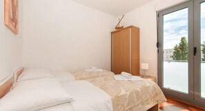 A hotel room with a bed, a wardrobe, a nightstand with a lamp, and a view through a glass door. - Apartments Nikolina - Comfort Two Bedroom Apartment (Split)