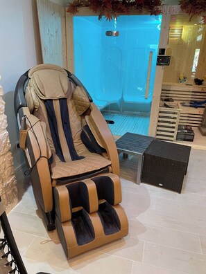 Uma cadeira de massagem com apoio para os pés, uma mesa pequena e um banco de madeira em um ambiente relaxante de spa.