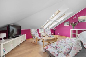 Ein modernes Schlafzimmer im Loftsstil mit einem Oberlicht, einem Flachbildfernseher, einer blumigen Tagesdecke und einem Holzstuhl.
