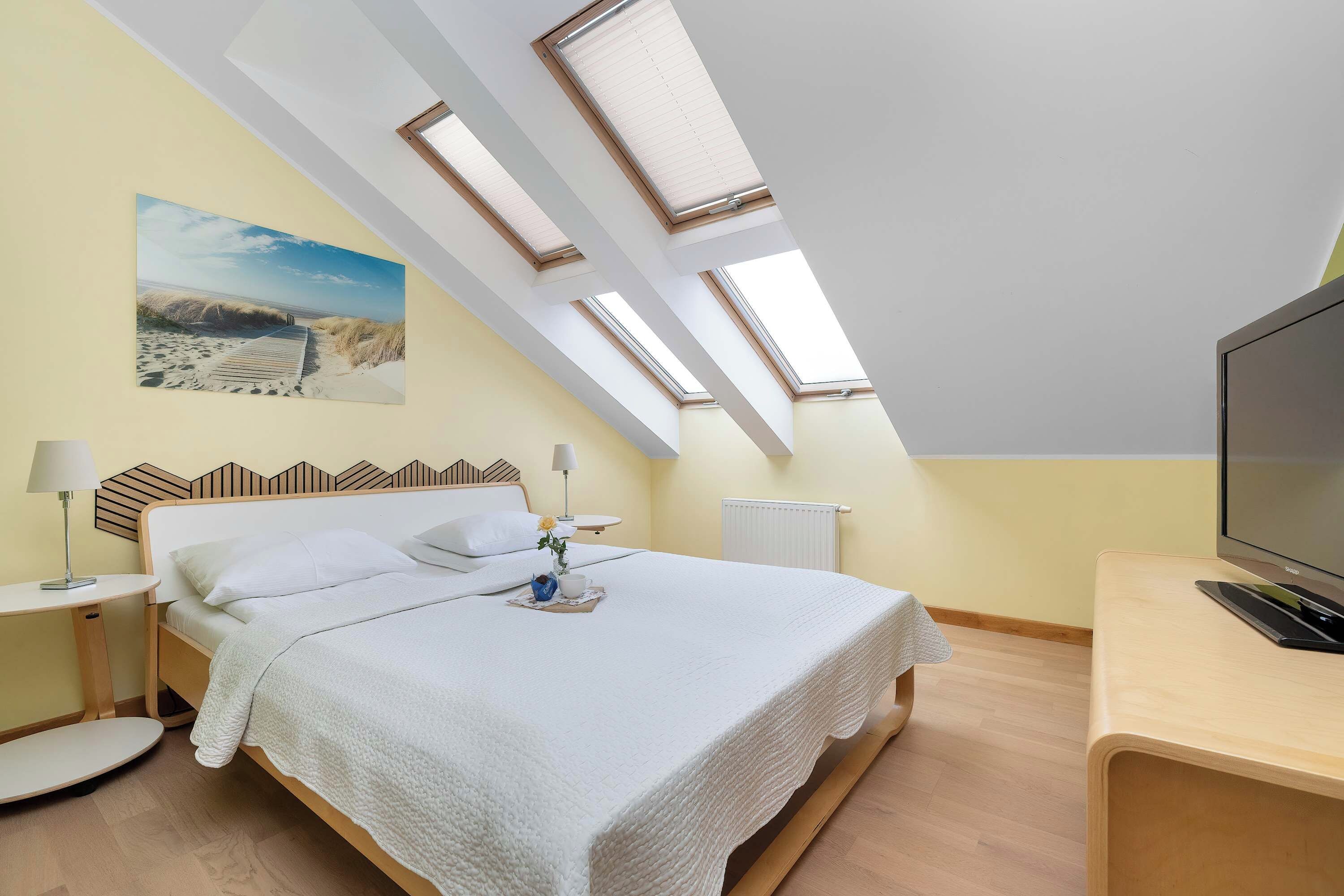 A bedroom with a bed, bedside tables, a TV, a radiator, and skylights.