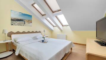 A bedroom with a bed, bedside tables, a TV, a radiator, and skylights.