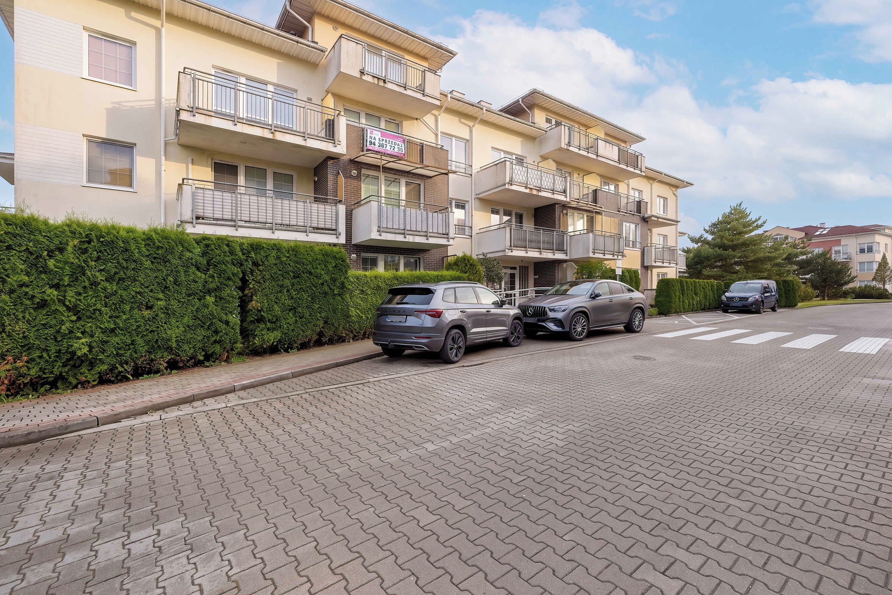Ein mehrstöckiges Wohngebäude mit Balkonen, einer gepflasterten Auffahrt und abgestellten Autos.
