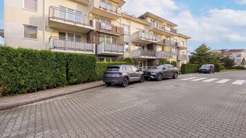 A multi-story residential building with balconies, a paved driveway, and parked cars.
