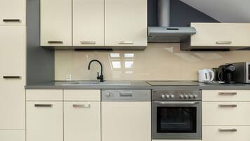 A modern kitchenette with white cabinets, a sink, an induction cooktop, and a built-in oven. The kitchen has a light countertop and a minimalist design.