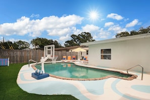 Ein Garten mit Pool, Basketballkorb und eingezäunter Liegebereich mit Liegestühlen.