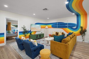 Ein modernes Wohnzimmer mit Wandgemälde in fröhlichen Farben, einer Sofagarnitur, einem Couchtisch und einem Fernseher.