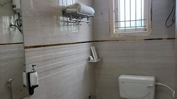 A small bathroom with a toilet, a shower, a window with bars, a towel rack, and a mirror.