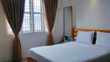A hotel room with a bed, curtains, a bedside table, a mirror, and a wall-mounted light fixture.